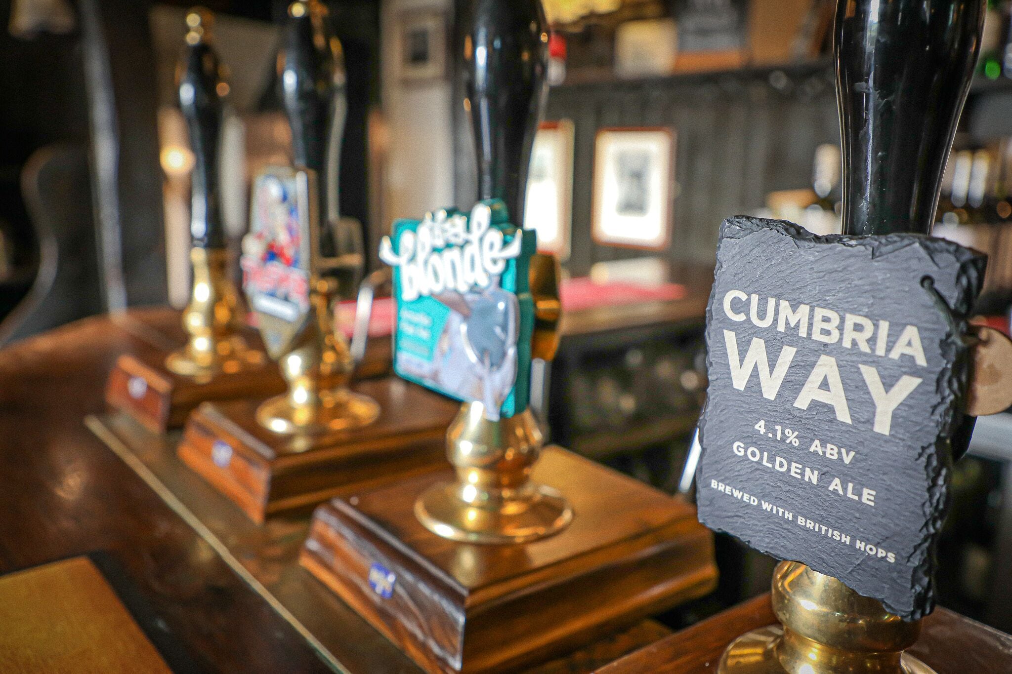 A bar with multiple beer taps, including one labeled 'Cumberland Way 4.1% ABV Golden Ale'.