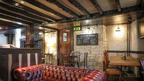 A cozy interior with a leather sofa, stone walls, wooden beams, and a chalkboard listing upcoming events. - Queens Head Inn (Penrith)