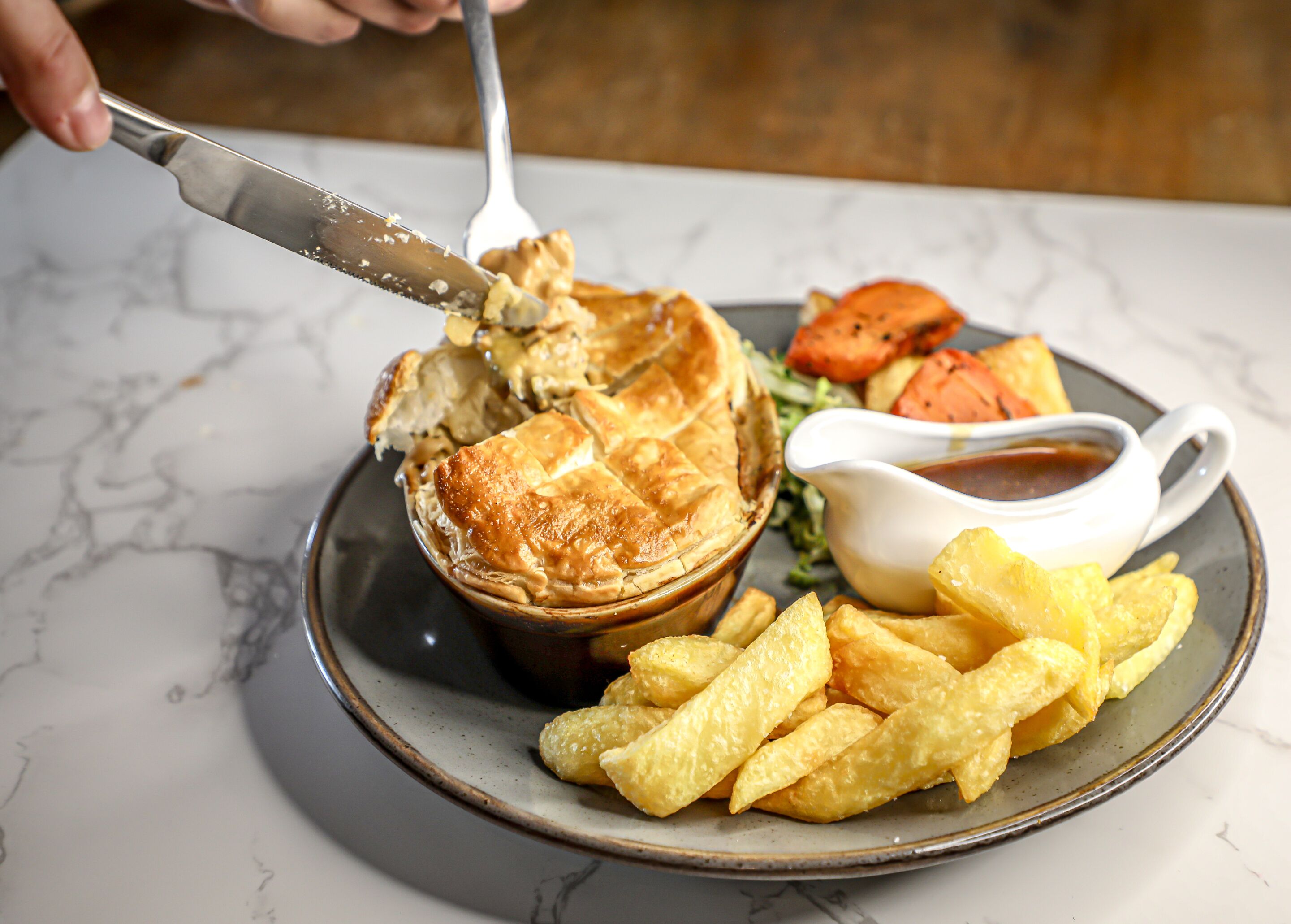 A pie with a fork and knife, accompanied by fries and a small bowl of sauce on a plate.