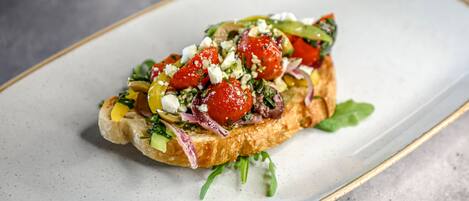 A plate with a sandwich topped with tomatoes, greens, and cheese.