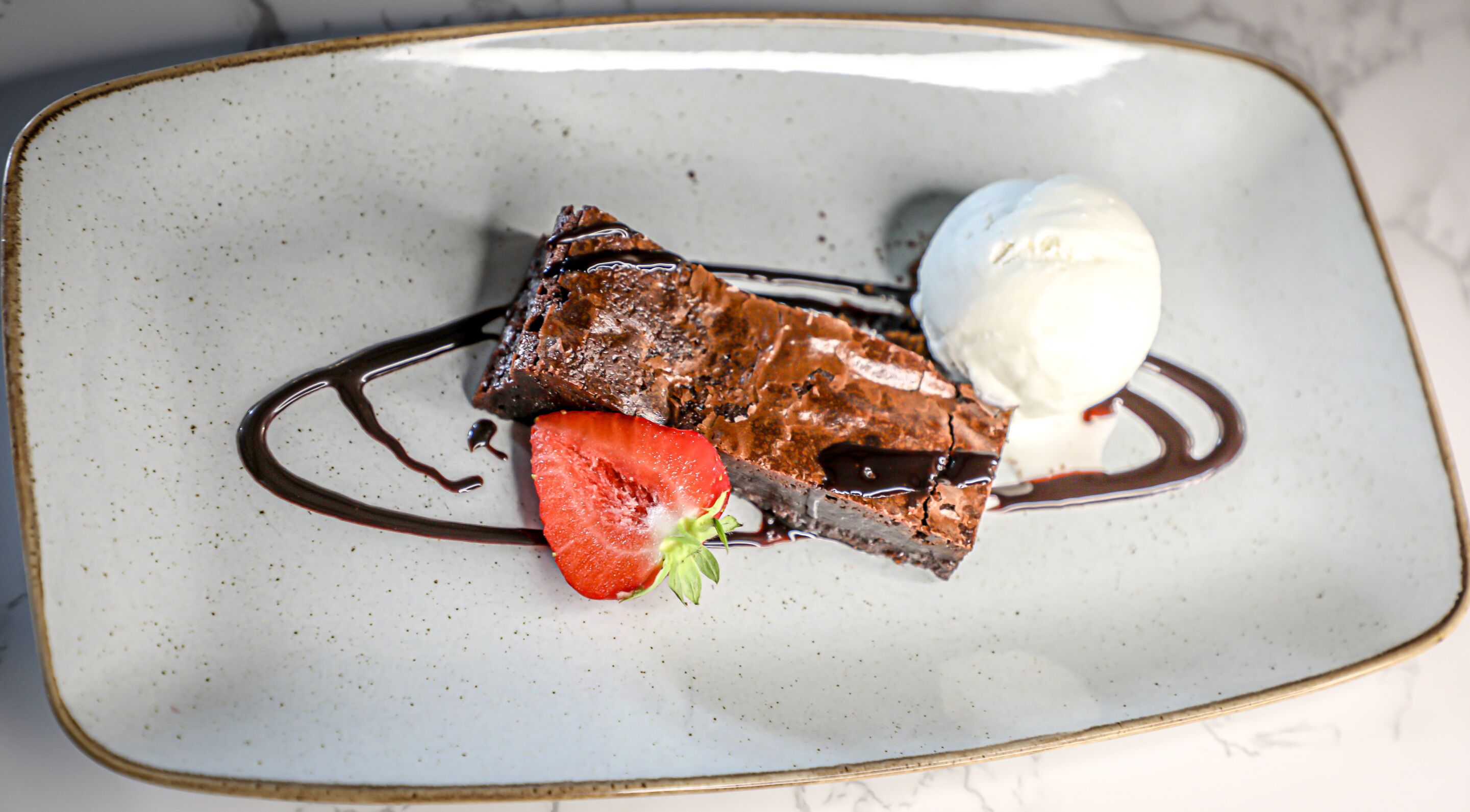 A dessert plate with a piece of chocolate cake, a scoop of ice cream, and a strawberry.