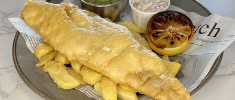 A plate of fish and chips with a side of mushy peas and tartar sauce, served on a newspaper.