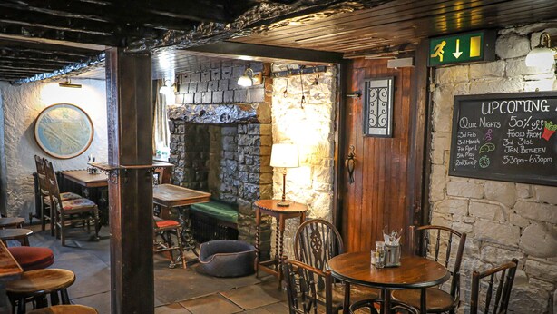 A cozy restaurant interior with stone walls, wooden furniture, and a chalkboard menu. - Queens Head Inn (Penrith)