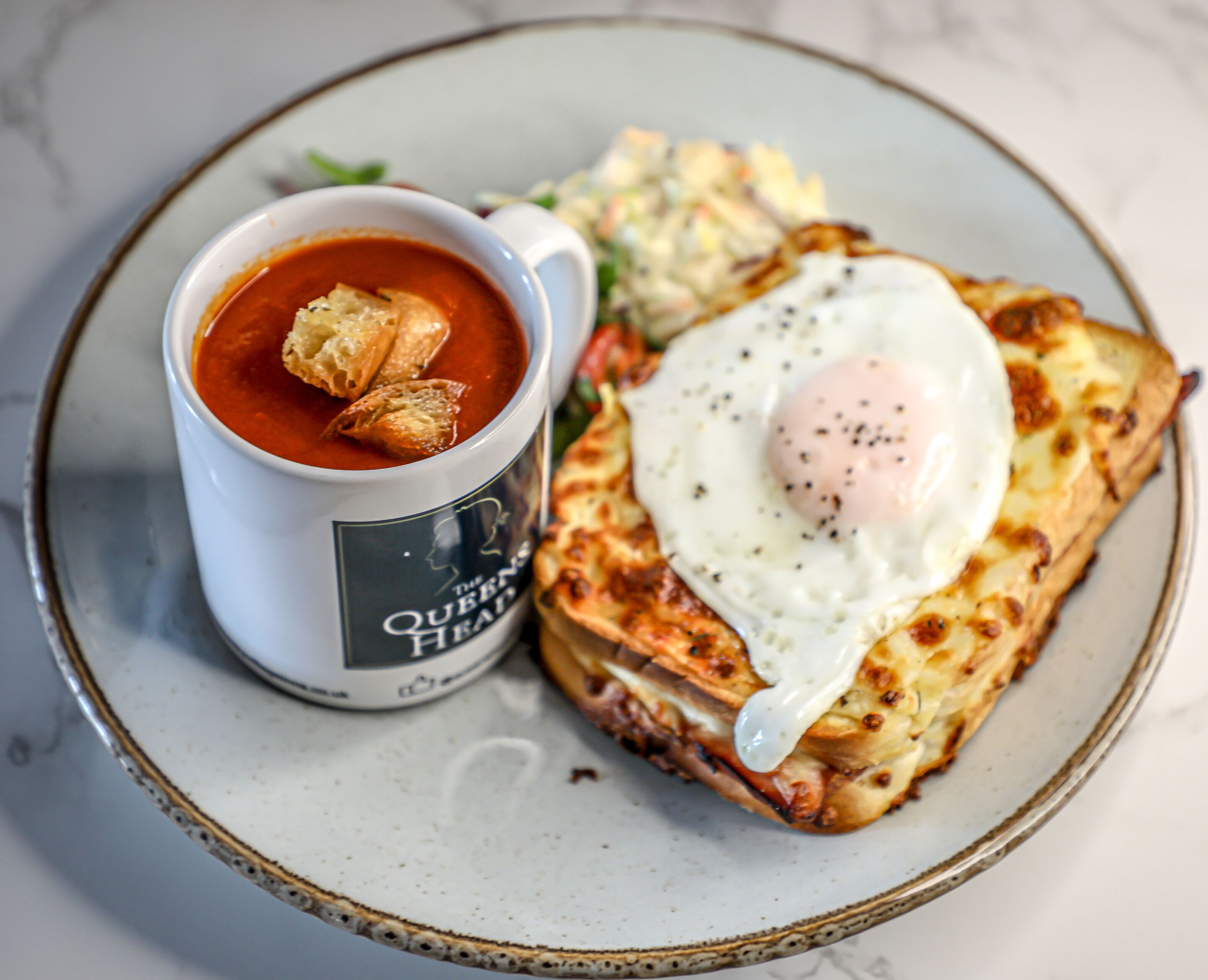 A plate with a poached egg on toast, a cup of tomato soup, and a side salad.