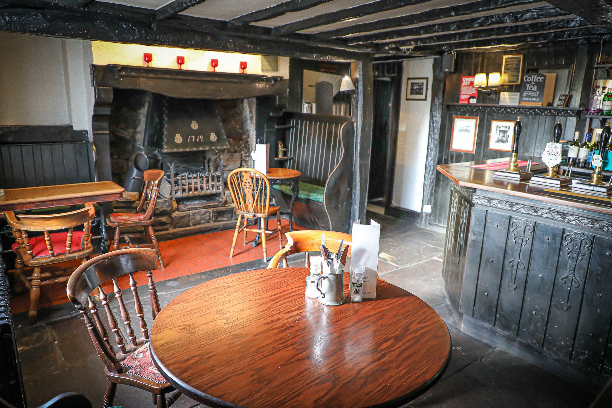 A cozy pub interior with a wooden table, chairs, a bar area, and a fireplace.