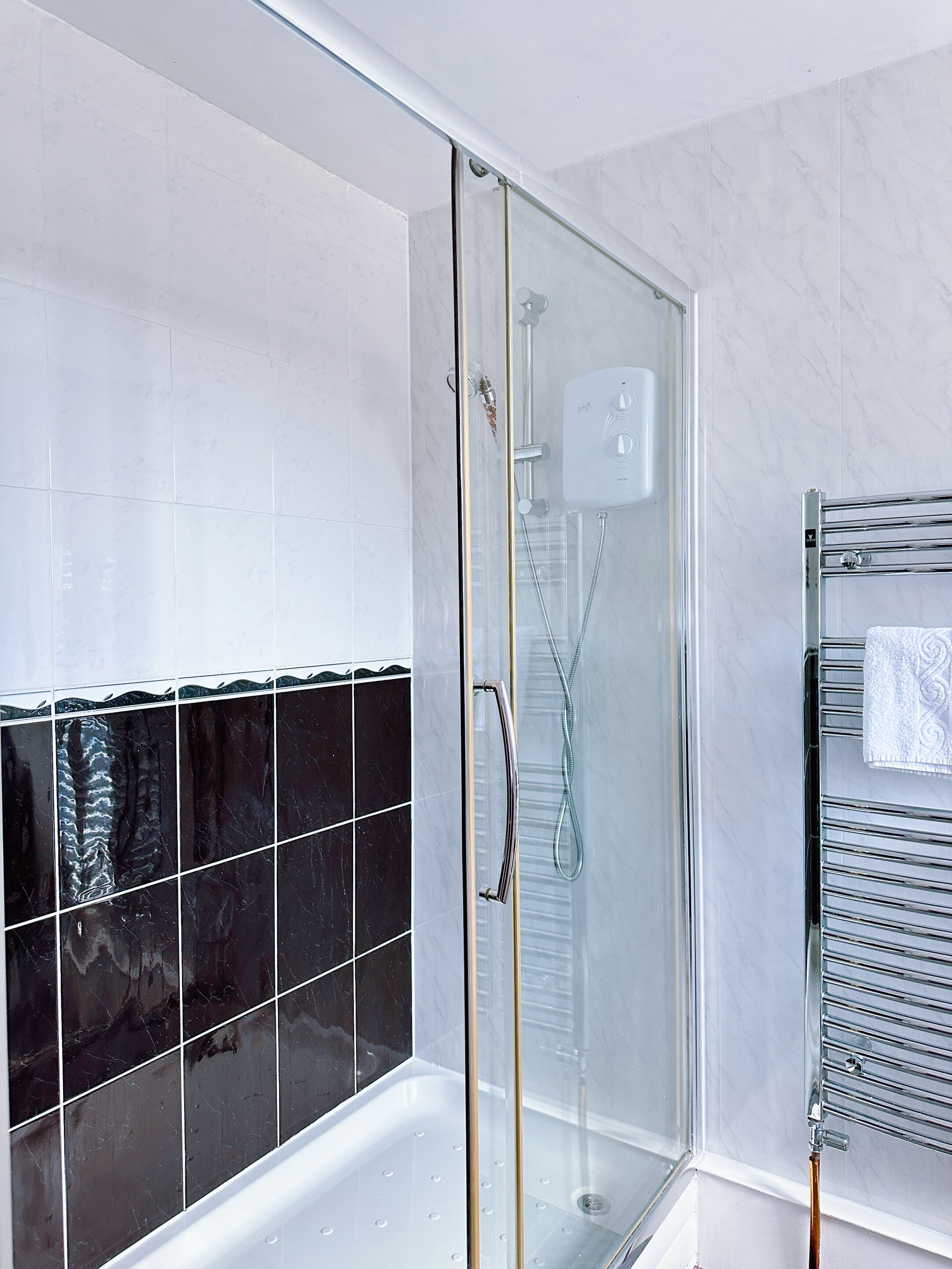 A modern bathroom with a glass-enclosed shower, a white tiled wall, and a black tiled accent wall.