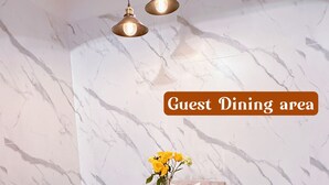 Een eetgedeelte voor gasten met een marmeren wand, een houten tafel gedekt met borden, bestek en een vaas met gele bloemen.