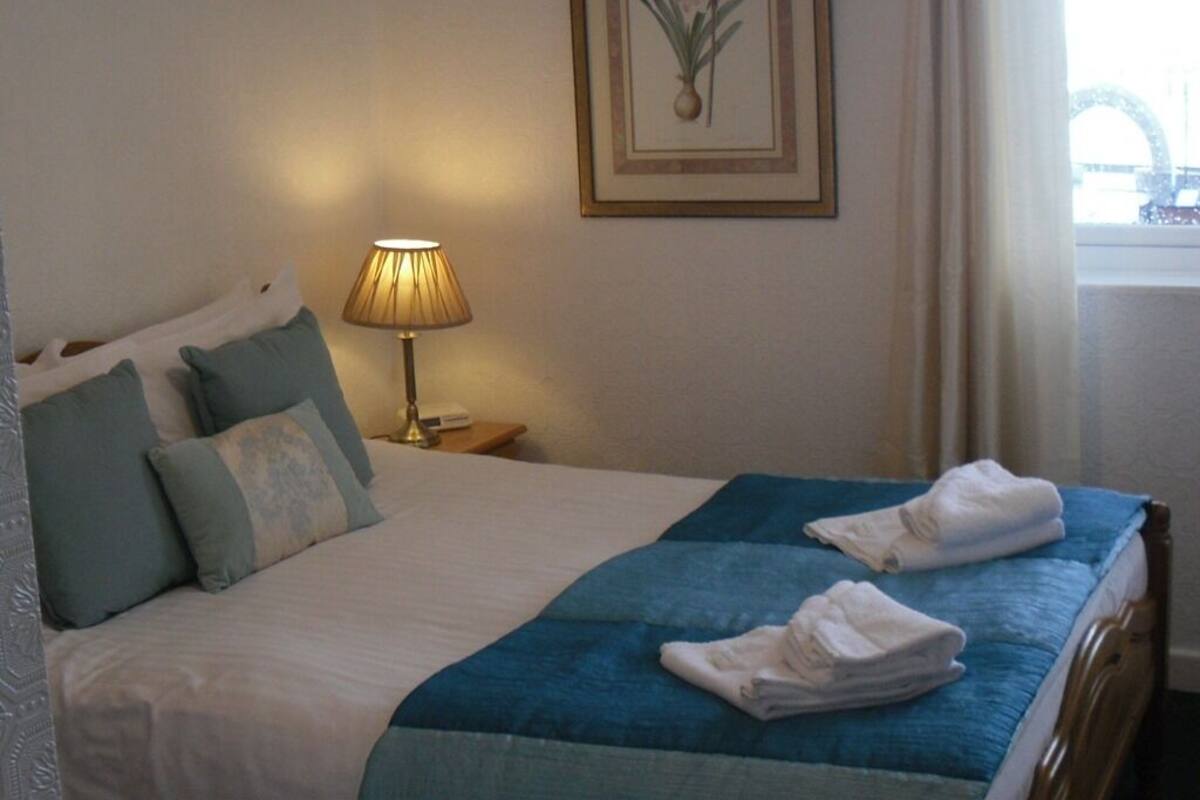 Un lit bien fait, avec une literie bleue et blanche, une lampe sur une table de chevet et un tableau encadré au mur.