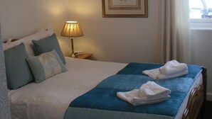 A neatly made bed with blue and white bedding, a lamp on a bedside table, and a framed picture on the wall.