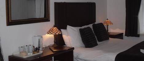 A hotel room with a large bed, bedside tables, a coffee maker, and a TV on the wall.