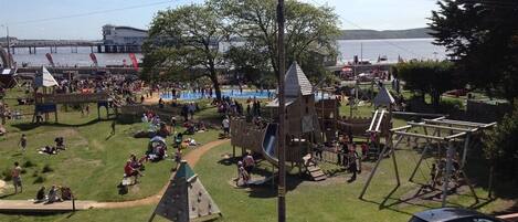 Un parque con áreas de juegos infantiles, zonas de picnic y vistas a un cuerpo de agua.