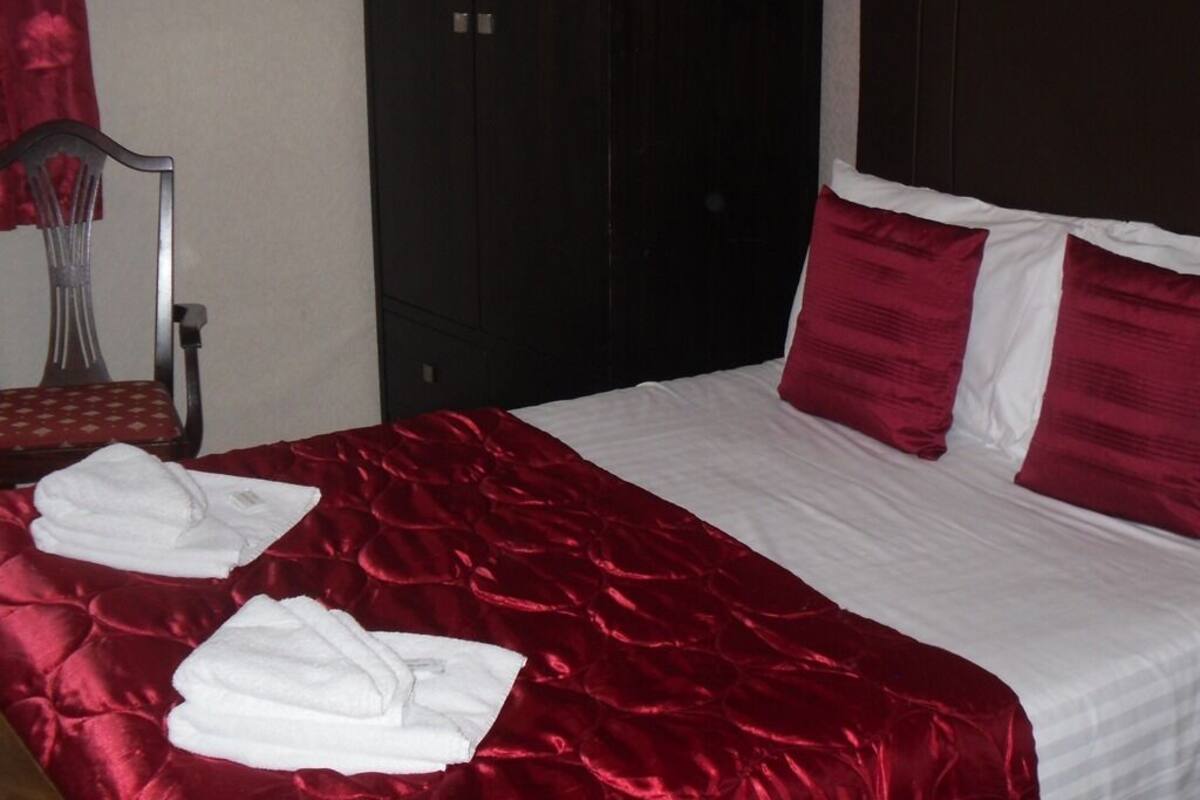 Une chambre d’hôtel avec un grand lit, une literie rouge et blanche, et deux serviettes blanches posées sur le lit.