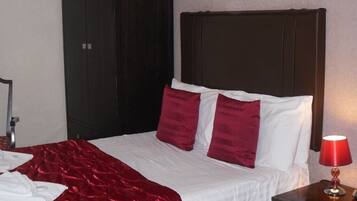 Habitación de hotel con una cama grande, cabecera oscura y una lámpara roja sobre una mesita de noche de madera.