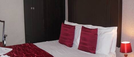 A hotel room with a large bed, a dark headboard, and a red lamp on a wooden nightstand.