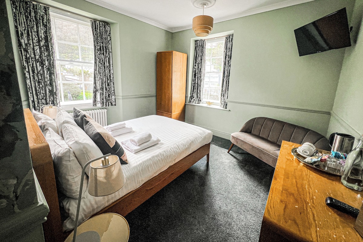 A hotel room with a bed, a wooden nightstand, a seating area, and a television mounted on the wall.
