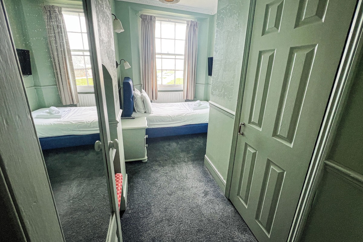 A room with a bed, a window with curtains, a door, and a carpeted floor.