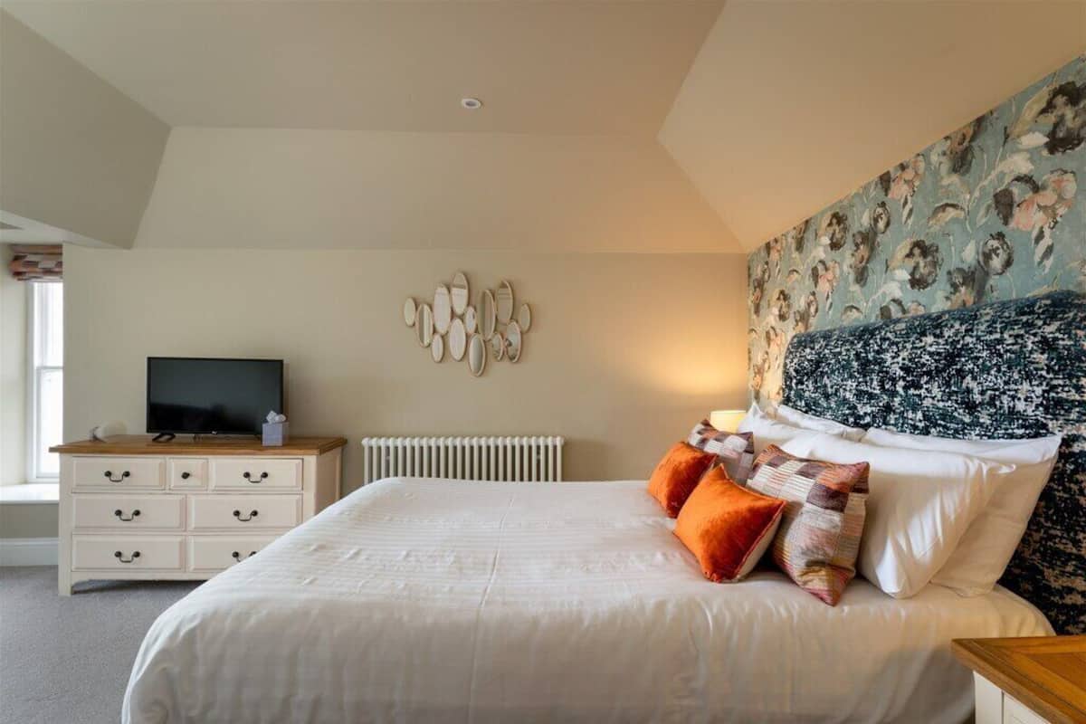 A bedroom with a large bed, a dresser, a television, and a decorative wall.