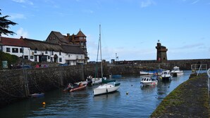 A harbor with boats docked, a lighthouse, and a building with a thatched roof.