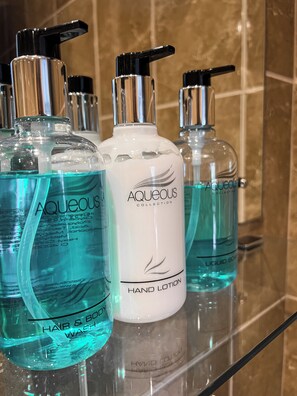 Uma prateleira no banheiro com vários loções para as mãos e um produto de limpeza para cabelo e corpo.