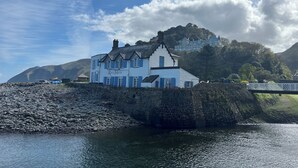 A white building with blue shutters labeled "Rock House" by a rocky shore with a clear sky.