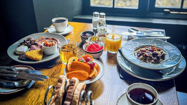 A breakfast table with various dishes, including eggs, beans, and toast, and a window with a view of buildings.