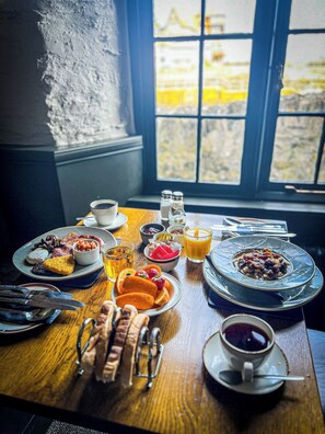 A breakfast table with various dishes, including eggs, beans, and toast, and a window with a view of buildings. - Rock House Hotel (Lynmouth)
