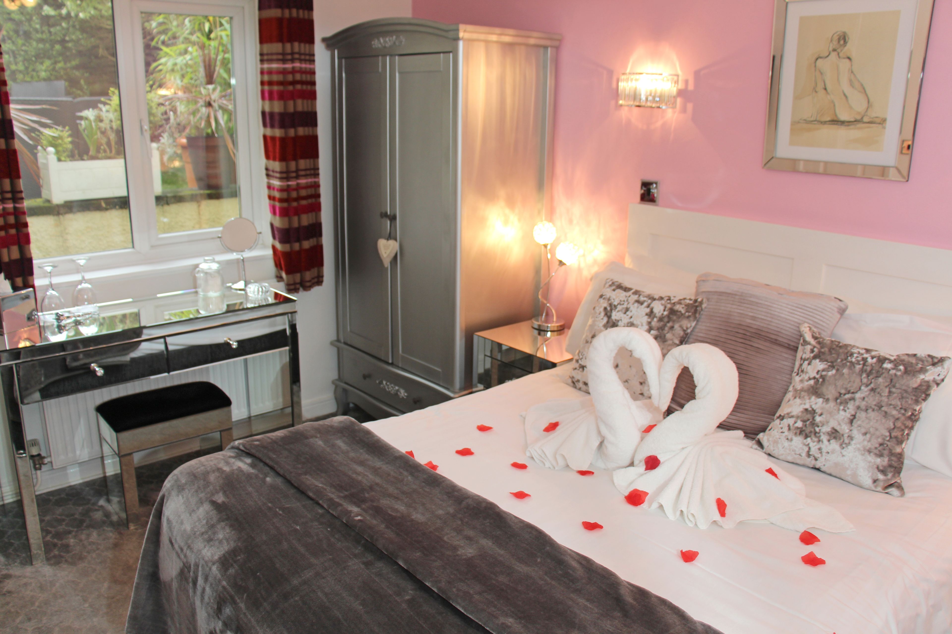 A bedroom with a bed, a wardrobe, a vanity with a mirror, and a window with curtains.