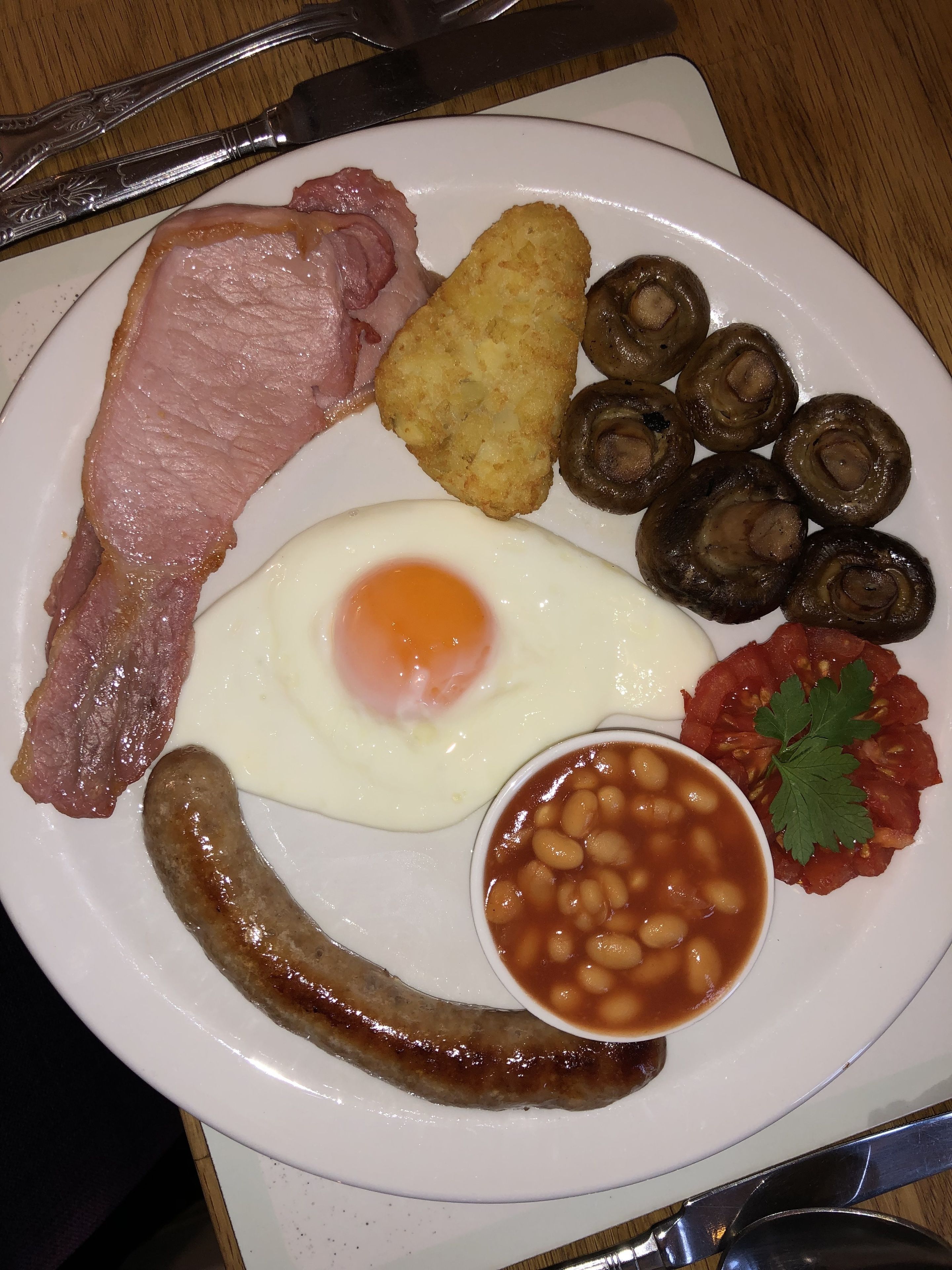 Une assiette de nourriture pour le petit-déjeuner comprenant du bacon, des saucisses, des œufs, des champignons, des haricots et des tomates.