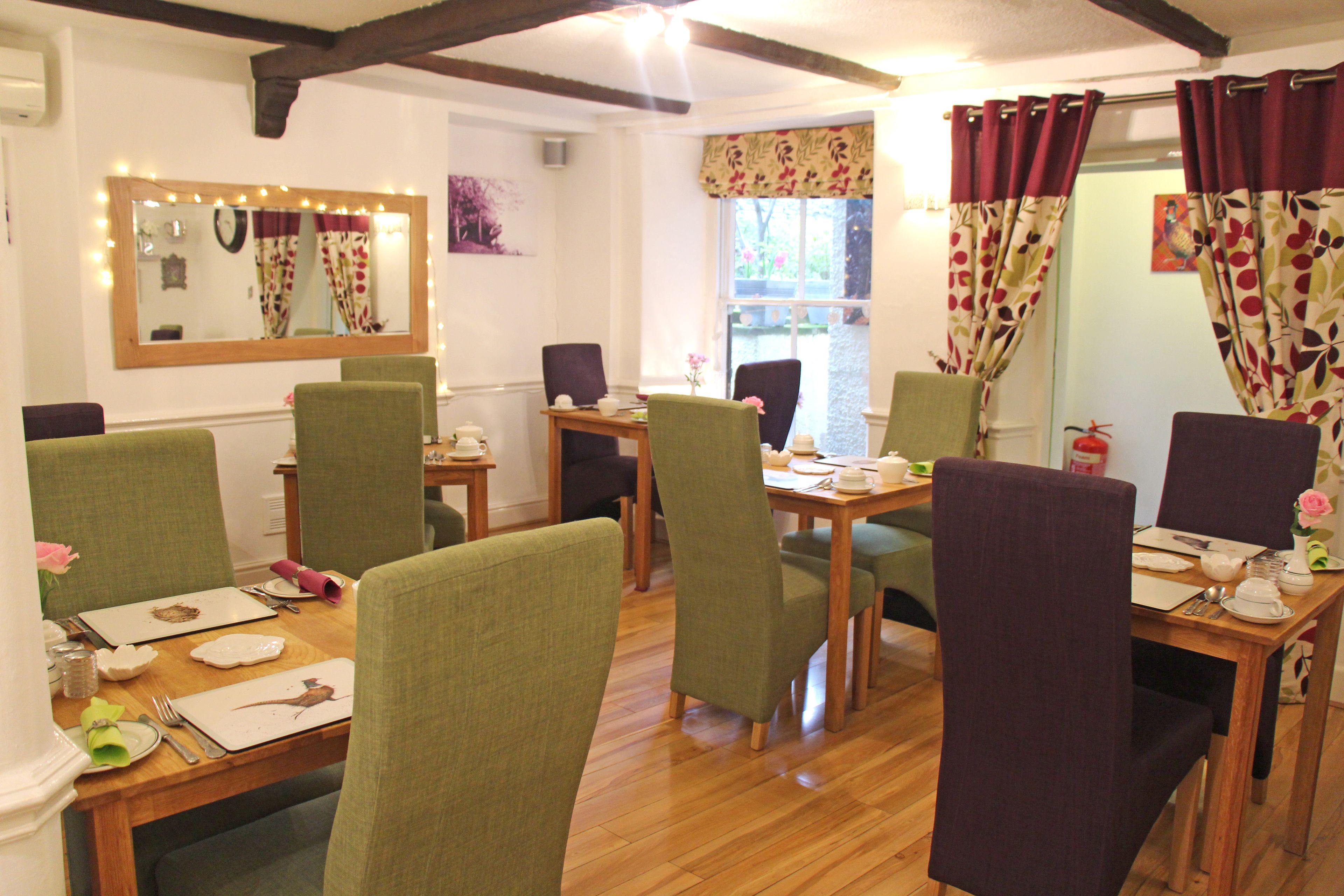 A dining area with wooden tables and chairs, a mirror with lights, and a window with curtains.