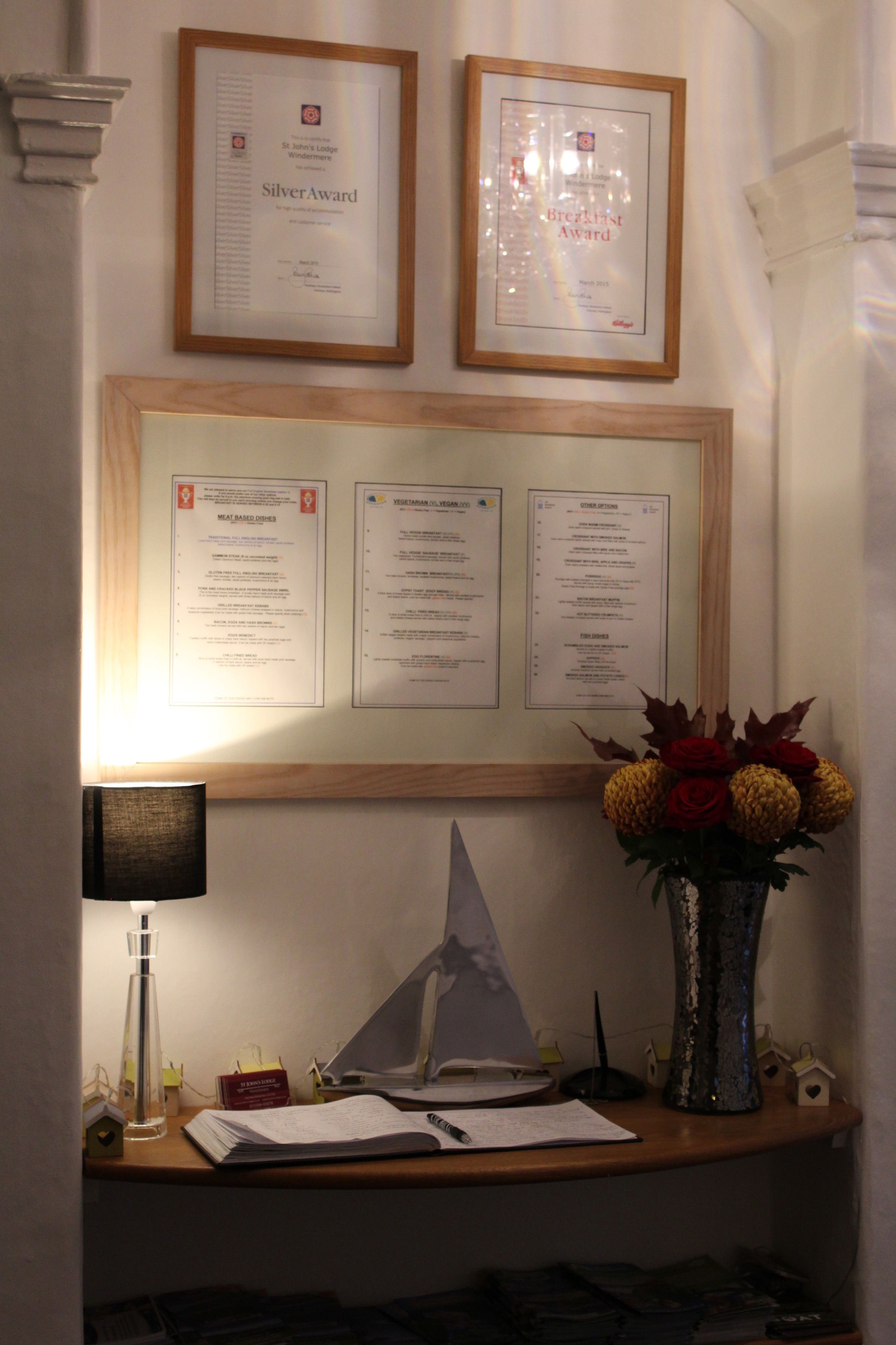 Framed awards, a menu board, a desk with a lamp, a vase with flowers, and a small house-shaped decoration.
