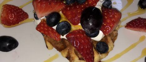 Un plato de comida con waffles cubiertos de fresas, arándanos y una cucharada de crema, rociados con jarabe.