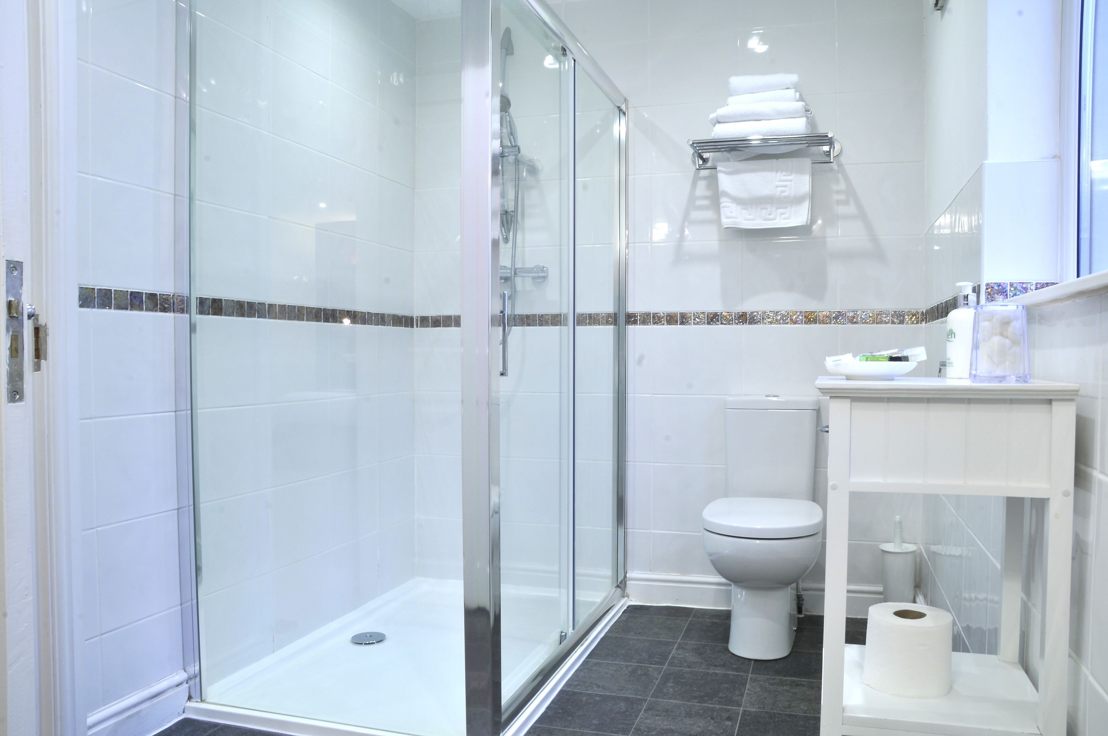 A modern bathroom with a glass-enclosed shower, a toilet, and a sink with a towel rack above.
