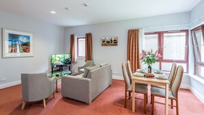 Una sala de estar con un sofá, dos sillones, una mesa de comedor con sillas, un televisor y un cuadro en la pared.