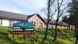 Señal para High Range Lodge con un diseño de montaña y águila, rodeada de césped y flores amarillas.