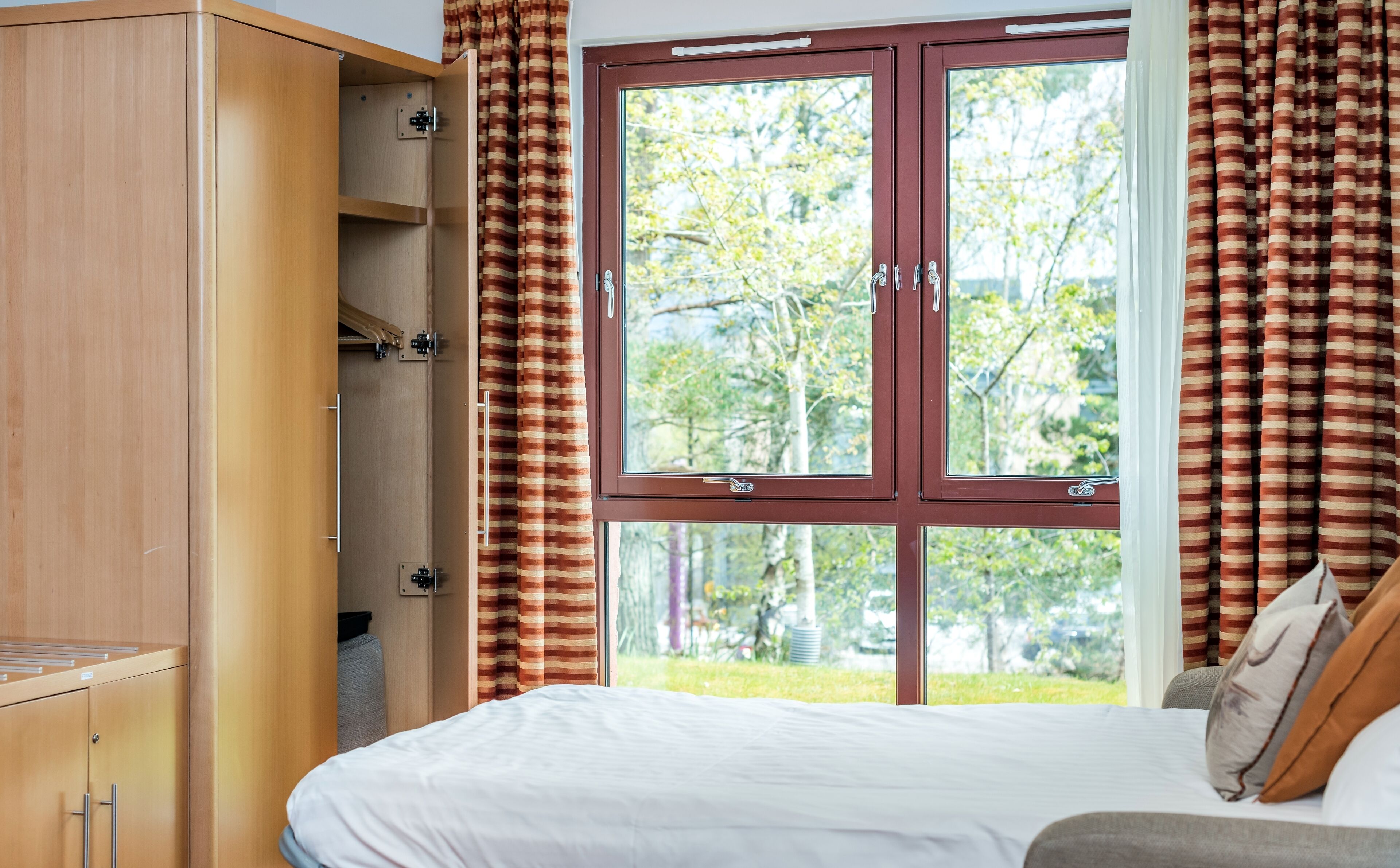 Un dormitorio con cama, armario y ventana con cortinas.