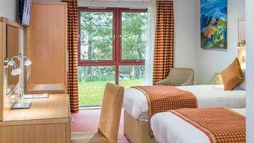 A hotel room with a desk, two beds, a chair, and a large window with curtains.