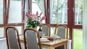 Una mesa de comedor con cuatro sillas, un jarrón de flores, una botella de vino y un vaso de agua.