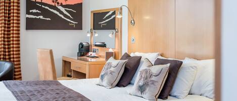 Una habitación de hotel con cama, mesita de noche, escritorio, silla y un cuadro en la pared.