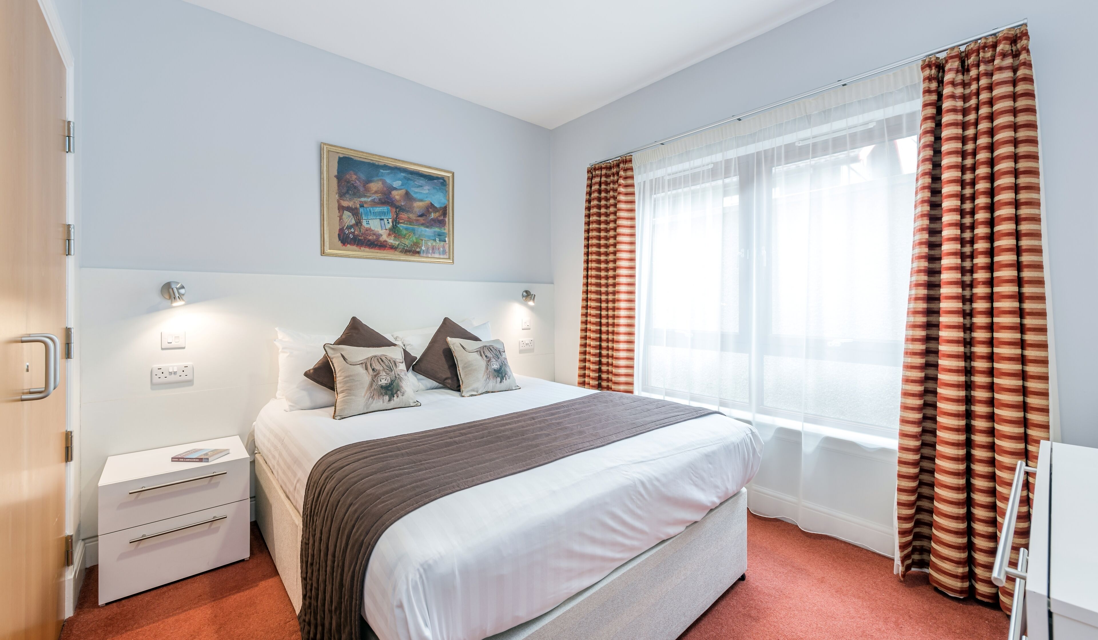 Ein Schlafzimmer mit einem Bett, Nachttischen, einem Gemälde und Vorhängen.