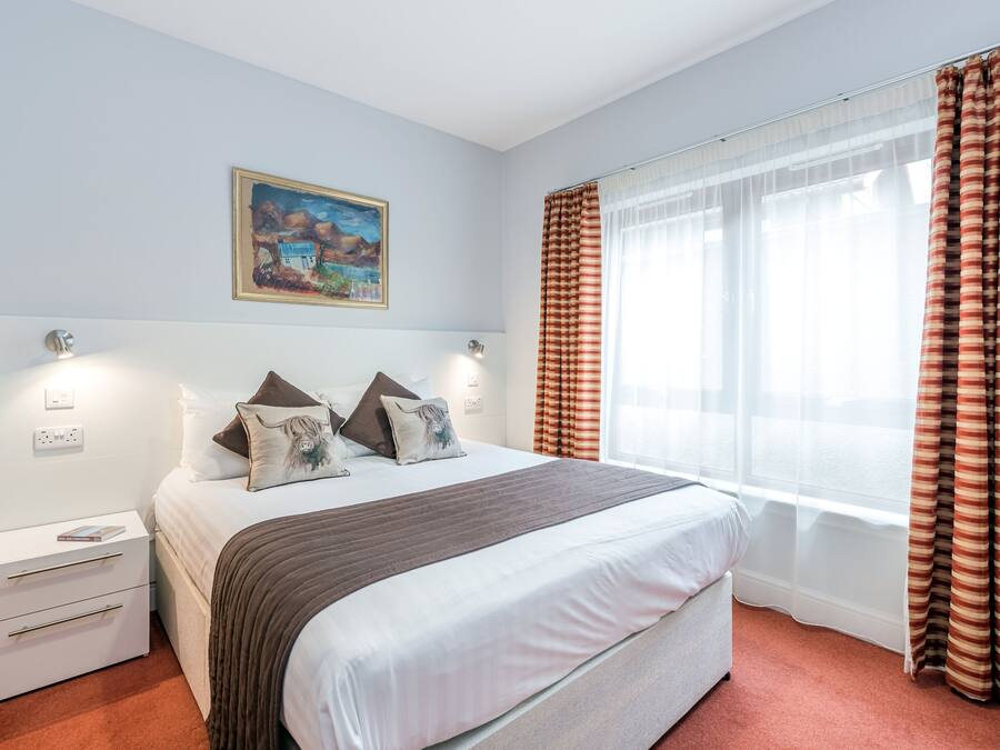 Ein Schlafzimmer mit einem Bett, Nachttischen, einem Gemälde und Vorhängen.