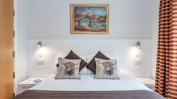 A hotel room with a bed, two pillows with animal prints, a painting on the wall, and a window with curtains.