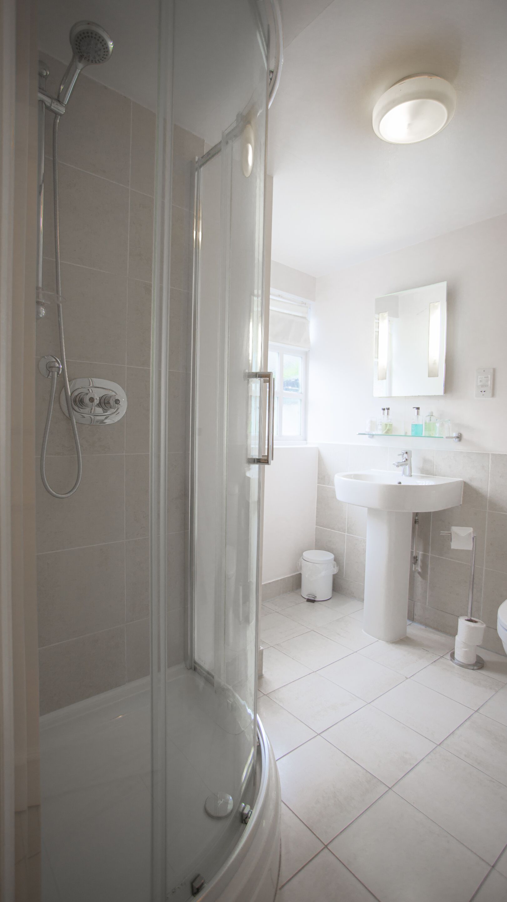 Un baño moderno con ducha envuelta en vidrio, un lavamanos blanco y un espejo sobre él.