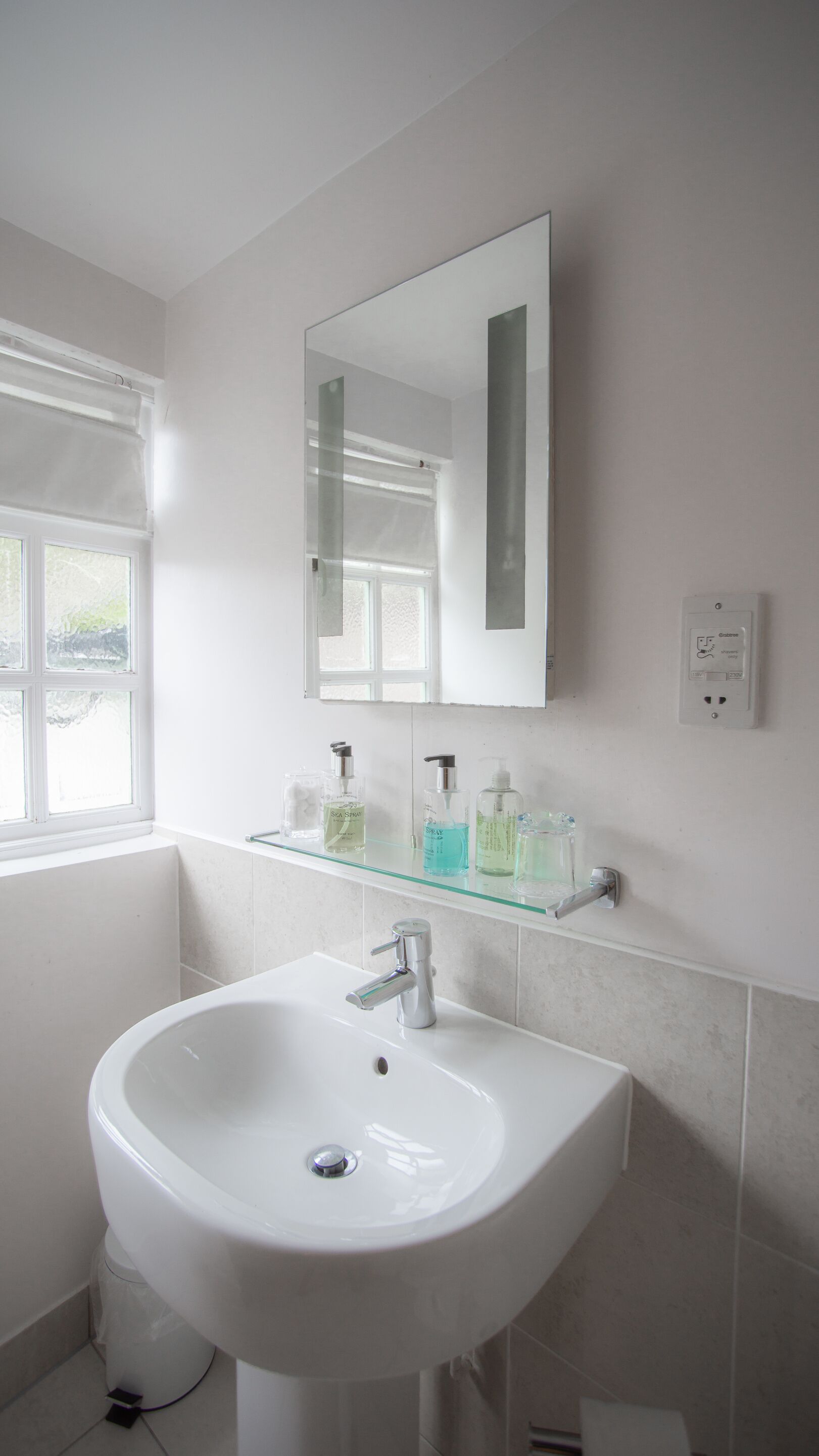 Un baño con un lavabo blanco, un espejo y una ventana.