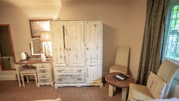A room with a large white wardrobe, a wooden desk with drawers, a chair, a small round table with a book, and a window with curtains.