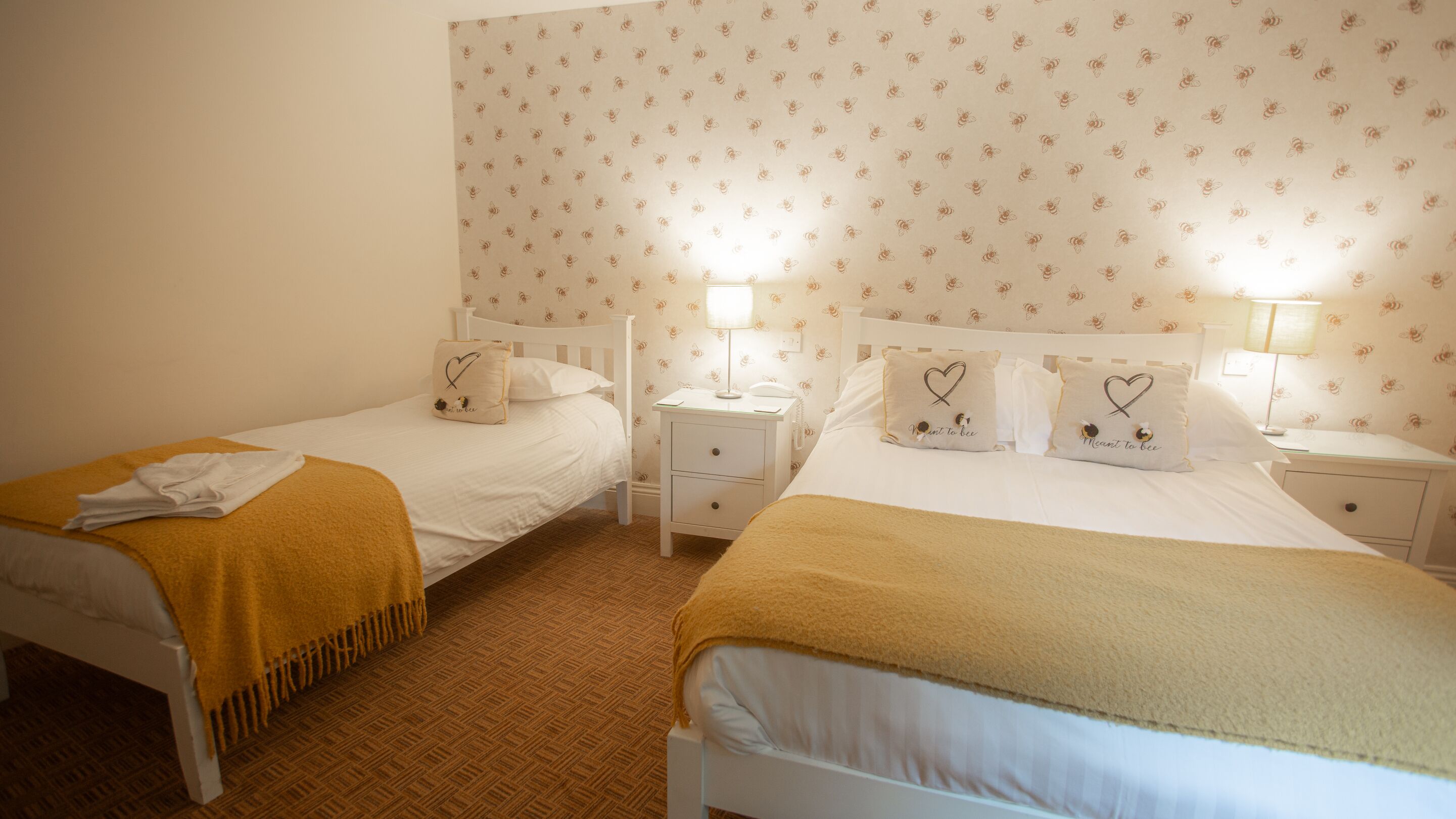Ein Hotelzimmer mit zwei Einzelbetten, jeweils mit Nachttisch und Lampe. Die Wände sind mit einem floralen Wandpapier gestaltet.