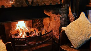 Une pièce chaleureuse avec une cheminée en pierre, une chaise en bois et un sol carrelé.