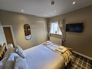 Un dormitorio con cama, espejo, ventana con cortinas, radiador y televisor en la pared.