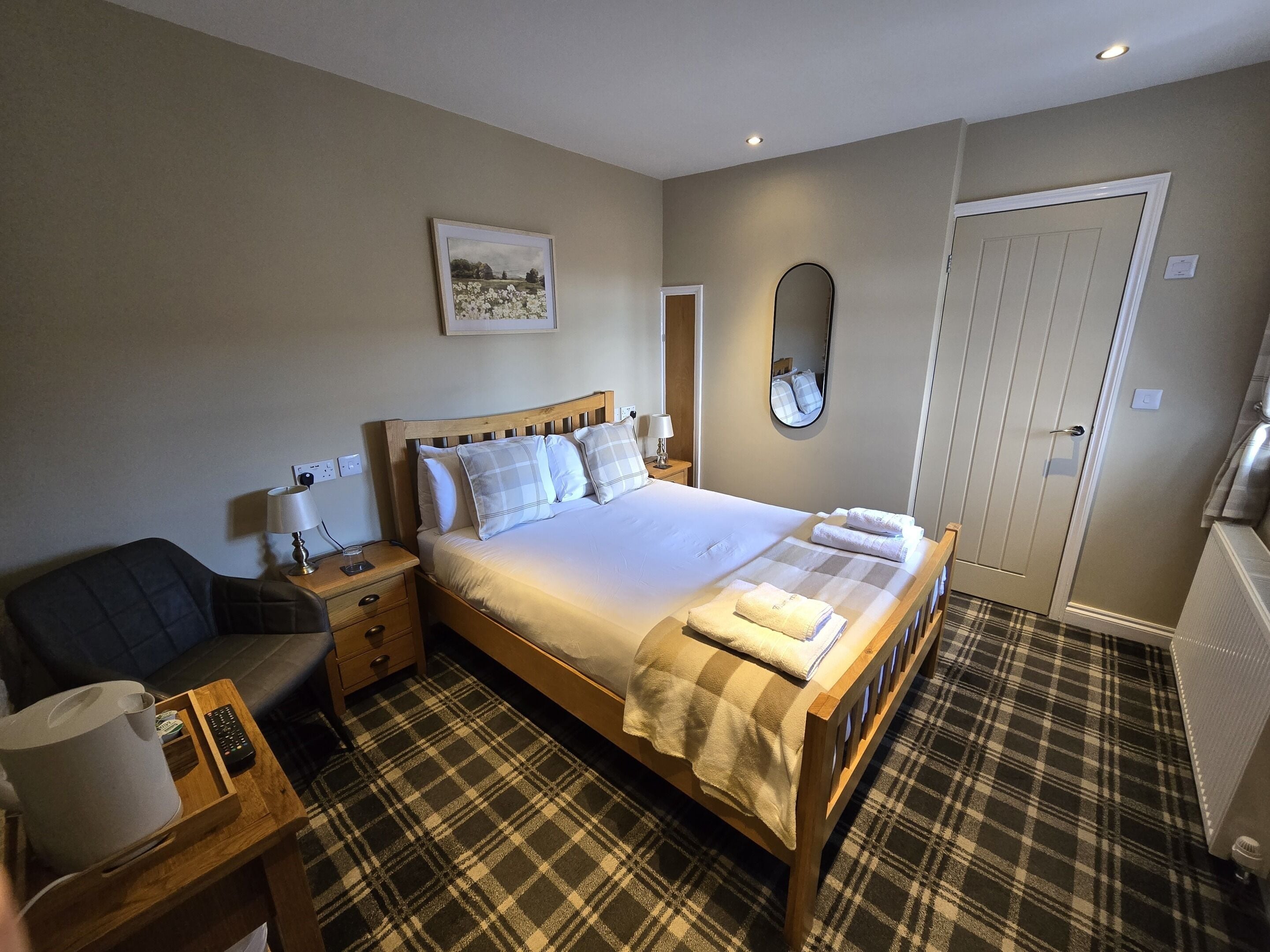 A neatly arranged hotel room with a bed, bedside tables, a chair, a mirror, and a door.