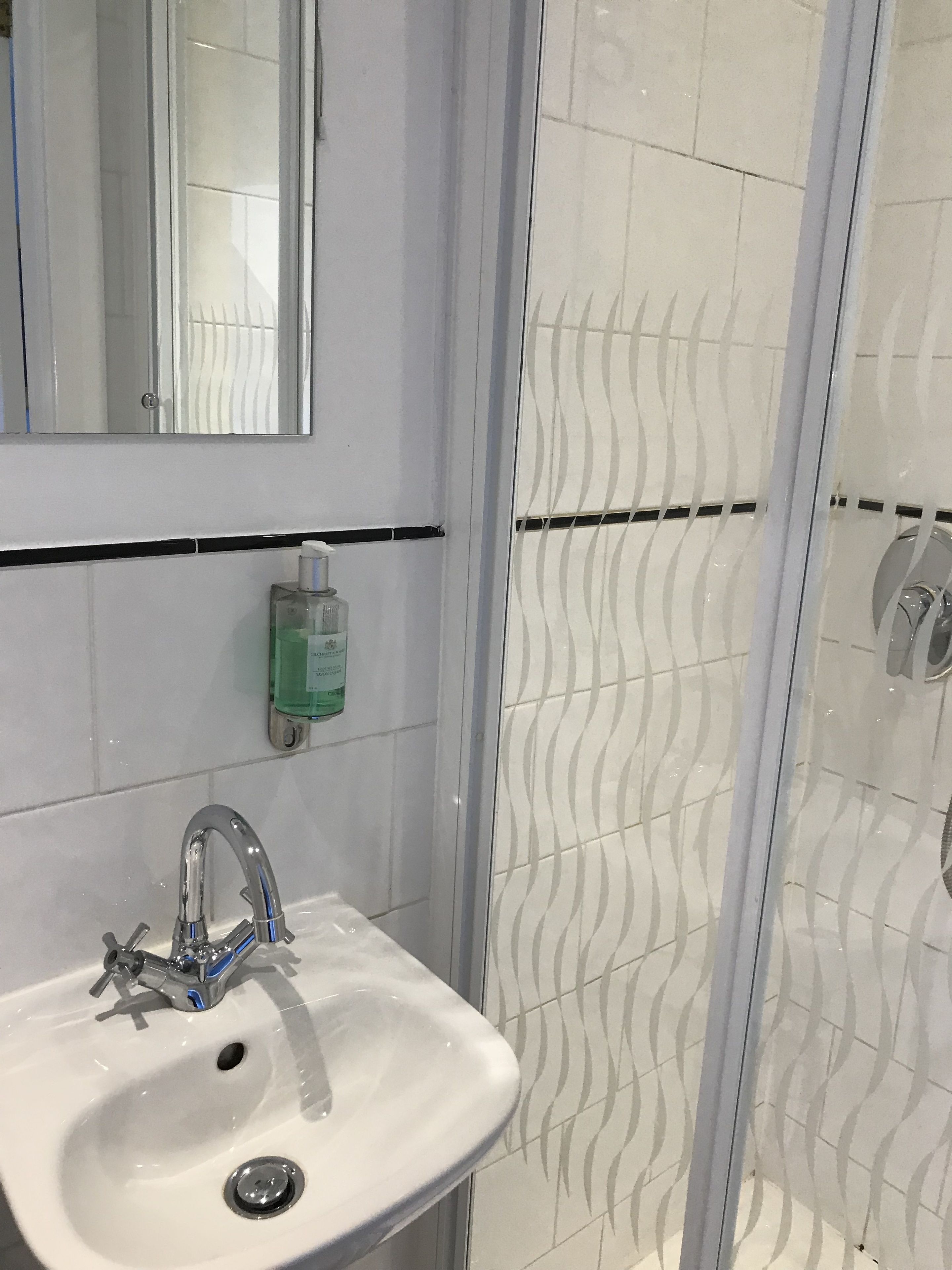 Ein Badezimmer mit einem weißen Waschbecken, einem Spiegel und einer Dusche mit einem wellenförmigen Fliesenspiegel.