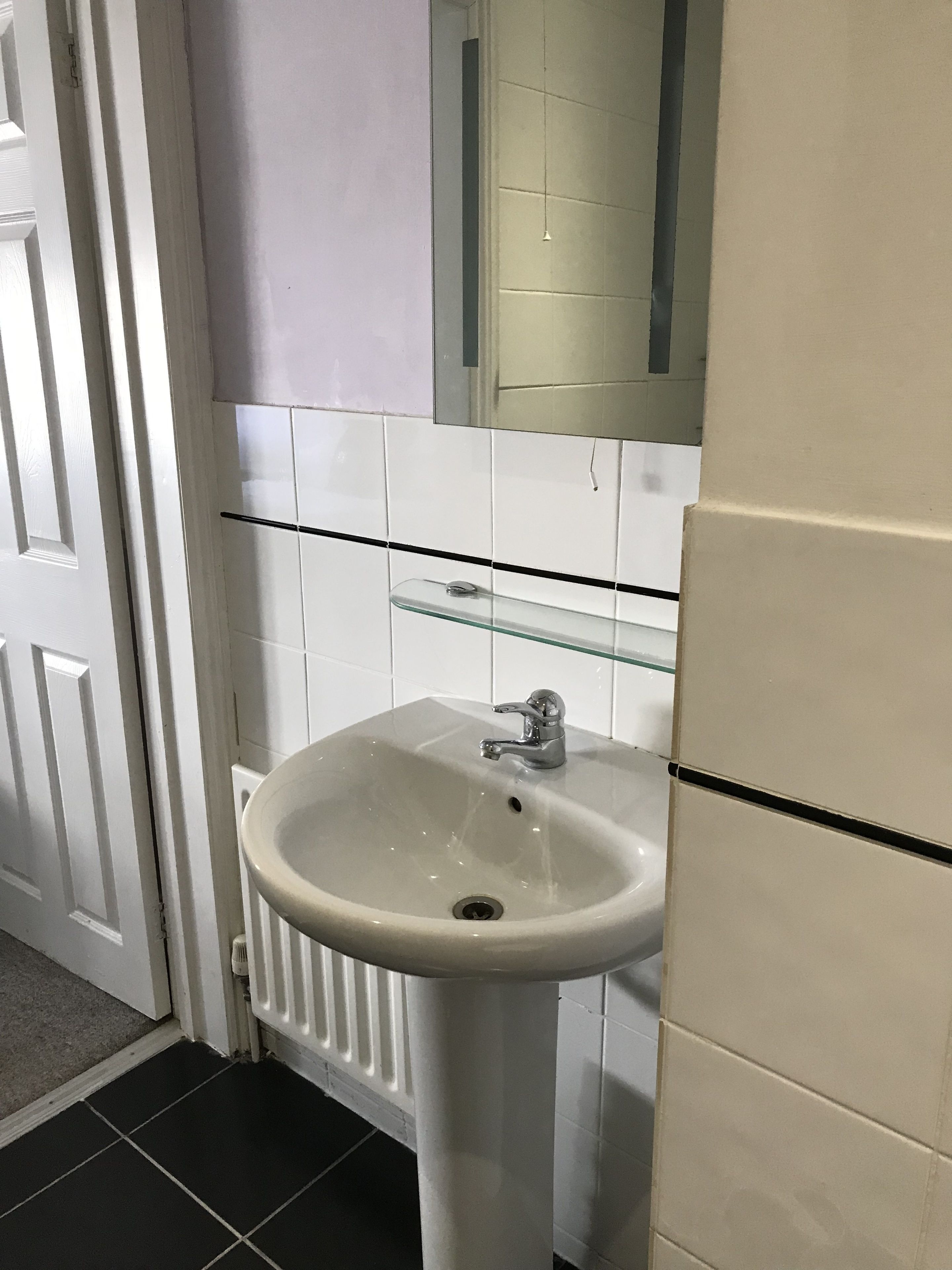 Ein Badezimmer mit einem weißen Waschbecken, einem Spiegel und einem Glasregal darüber.